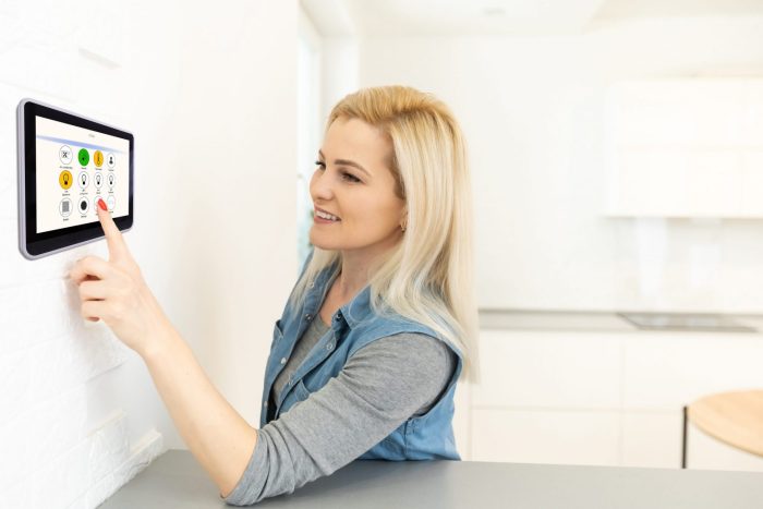 Photo of woman adjusting her thermostat at home illustrates blog: "Here’s Why You Shouldn’t Set Your Thermostat Too Low on Hot Days"