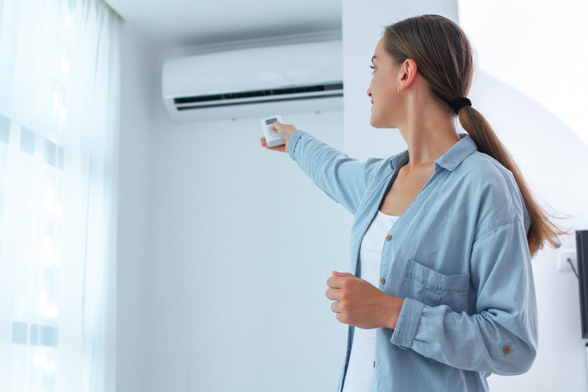 Photo of woman pointing remote control to AC illustrates blog: "What To Do if Your HVAC Smells Like Burning Plastic?"