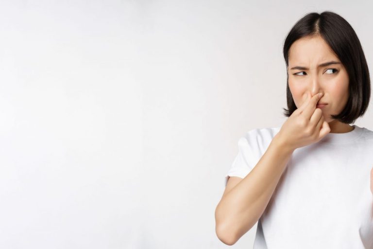 Woman pinching her nose illustrates blog "Should I Turn My AC Off if It Smells?"