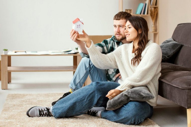 Couple in living room holding a small toy house.