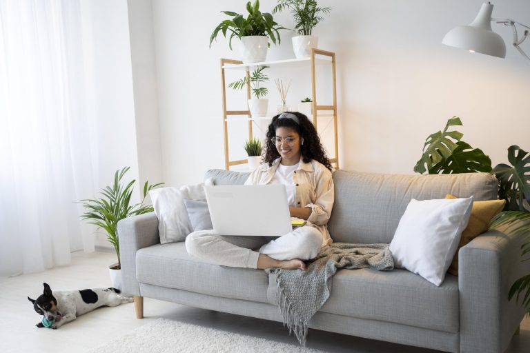 Woman sitting in living room with laptop illustrates blog "What Are the Most Common AC Condenser Unit Issues?"
