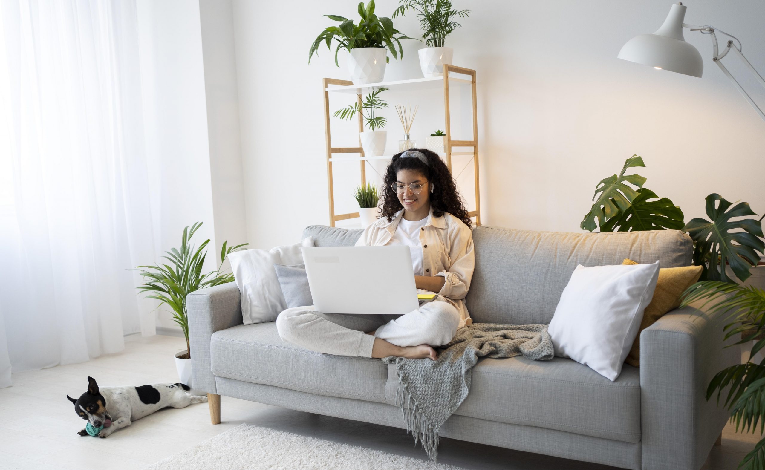 Woman sitting in living room with laptop illustrates blog "What Are the Most Common AC Condenser Unit Issues?"